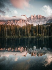 Vertical shot of a lake surrounded by a forest and Italian dolomites during the sunrise