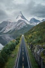 Vertical shot of a road surrounded by a lake and rocky hills on a foggy day in winter