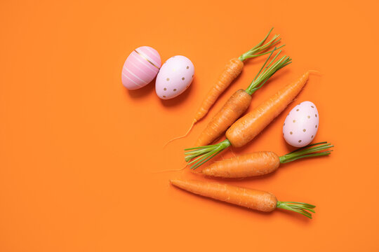 fresh spring carrot with easter eggs on an orange background. top view. copy space. flat lay.