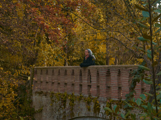 senior woman looking from a stone bridge. mature woman in autumn forest