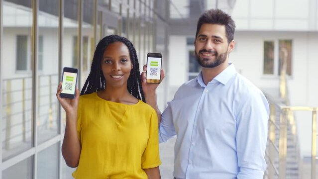 Multiethnic couple looking at camera showing vaccinated qr-code on cellphone