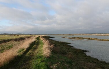 Fototapeta na wymiar Footpath by the river under a cloudy sky at Old Hall Marshes, Essex, UK