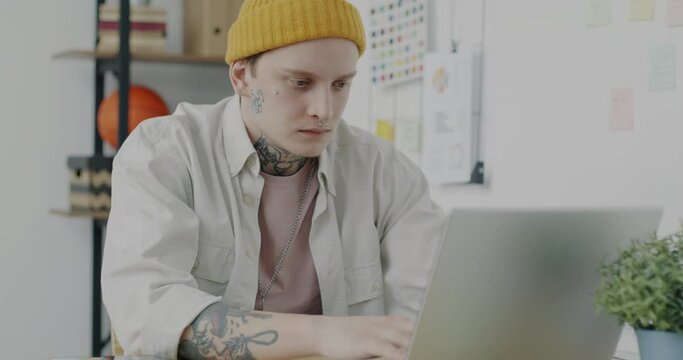 Portrait of young man wearing informal clothing working with laptop then massaging head suffering from headache in office. Health problems and job concept.