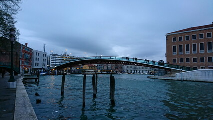 Venice, Italy - Apr 09 2018: Side view of the Ponte della Costituzione, Constitution Bridge, on a rainy day at dusk with pedestrians walking on it before the pandemic