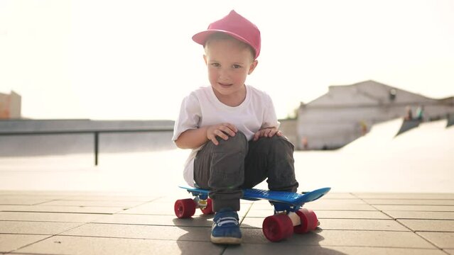 child boy close-up with a skateboard. boy in a red cap with a skateboard on the playground portrait. skateboarder child outdoors sun glare. kid skateboarder looking lifestyle at the camera