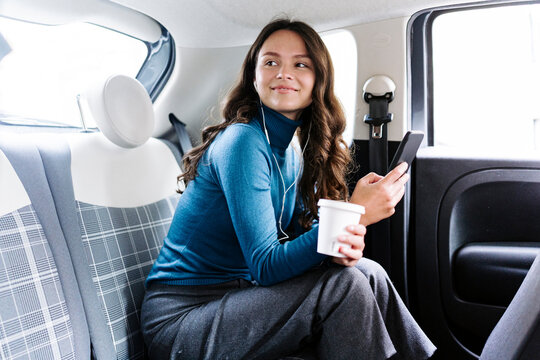 Smiling woman watching movie on tablet in earphones in car