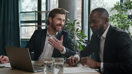 Two happy satisfied multiracial men diverse businessmen in office meeting talking laughing with laptop document partnership working with project Caucasian man executive manager African American worker