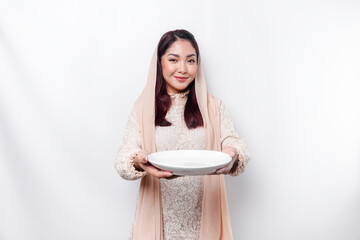 An Asian Muslim woman is fasting and hungry and holding utensils cutlery while looking aside thinking about what to eat