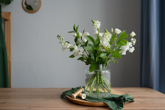Glass vase with bouquet of flowers on board near ribbons