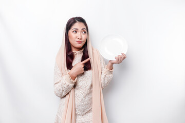 An Asian Muslim woman is fasting and hungry and holding utensils cutlery while looking aside thinking about what to eat