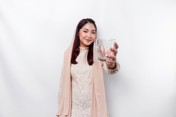 Joyful Asian Muslim woman wearing headscarf is drinking a glass of water, isolated on white background.