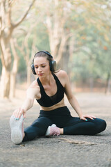 In an Autumn city park background, a stunning sportswoman in sportswear is smiling while stretching her body and performing flexibility exercises as a warm-up before a running workout.