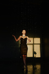 Water splash. A girl in black dress under the drops water. Wet clothes. Young woman enjoying relaxed.