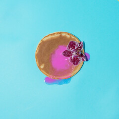 American pancake covered wih acrylic paint and decorated with a flower on a blue background. Creative food concept.