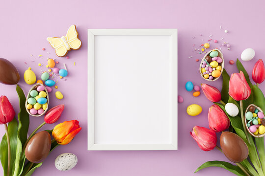 Easter sweets concept. Top view photo of vertical photo frame chocolate eggs with сolorful dragees butterfly cookie and tulips flowers on isolated lilac background
