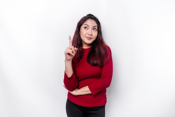 Excited Asian woman dressed in red, pointing at the copy space on top of her, isolated by white background