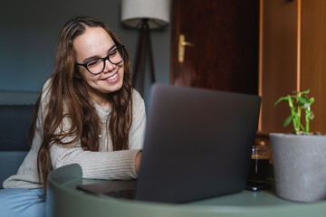 A young girl sitting at home while using laptop to study or do business while drinking coffee and using mobile phone