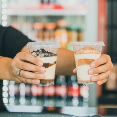 Close-up view of hands holding desserts in plastic cups