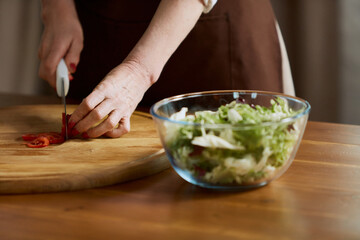 Close-up image of female hand cutting tomatoes on cutting board. Woman cooking healthy vitamin salad with fresh vegetables at home. Concept of family, relationship, retirement, lifestyle, happiness