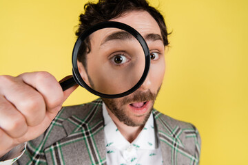Wide angle view of stylish man looking through magnifying glass isolated on yellow.
