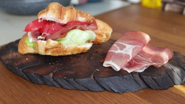 sliced prosciutto or jamon meat and croissant on wooden board in kitchen.