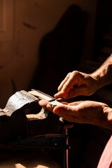 Close up of man's hands smoothing a piece of wood with a tool under the sunlight - concept of crafts