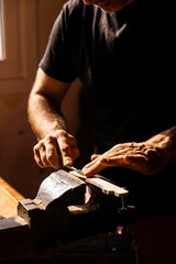Close up of man's hands smoothing a piece of wood with a tool under the sunlight - concept of crafts