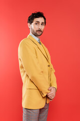Stylish charming guy in yellow jacket standing on coral red background.