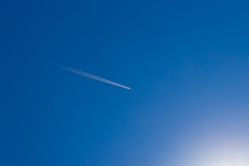 A plane flying over the clear blue sky, leaving a trail of wake.