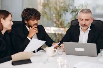 Focused businesspeople sitting at the table in conference room. Brainstorming during business meeting. Company executive and his colleagues working on new marketing strategy