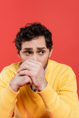 stressed man with clenched hands covering face and looking away isolated on coral.