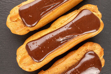 Three chocolate eclairs, close-up, on slate stone, top view.