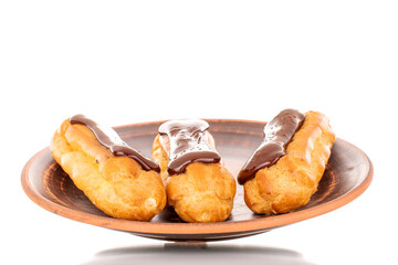 Three sweet chocolate eclairs on a clay saucer, close-up, isolated on white background.