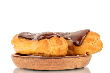 Two sweet chocolate eclairs on a wooden saucer, close-up, isolated on white background.