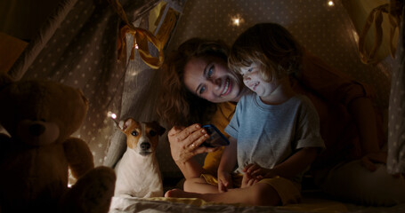 Joyful young mother taking care of her son. Beautiful woman watching cartoons together with her...