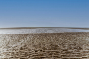 Maritime mudflat landscape with reflection of clouds in low tide water