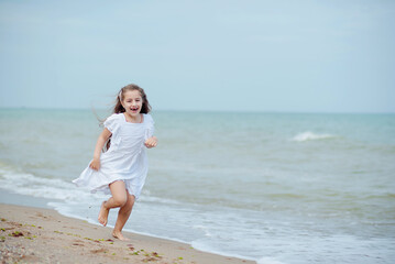 Fototapeta na wymiar Cute little girl running along the seashore against a clear blue sea and rejoices