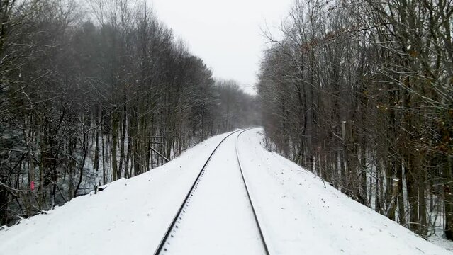 Drone shot view of train tracks in the winter surrounded by forest with falling snow in New York