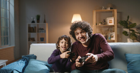 Funny south asian siblings are relaxing together, playing video games in front of tv, father and...