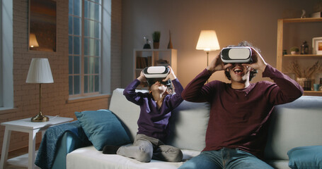 Funny south asian siblings or father and son with curly hair are trying virtual reality headsets, having fun playing video games - modern technologies, family time concept