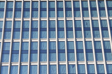 Glass facade of an office building with curtains on the windows in blue tones.