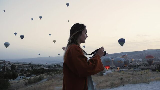 Happy young beautiful tourist, photographer woman using film camera to take picture of hot air balloons sky scenery.