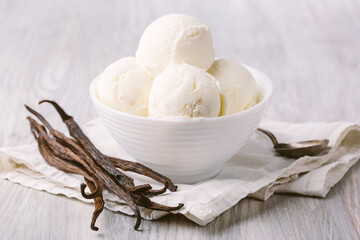 Food concept. Side view photo of ice cream balls in white bowl and dried vanilla beans on light wooden background