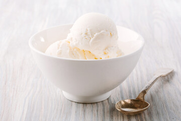 Food concept. Side view photo of ice cream balls in white bowl and spoon on light wooden background