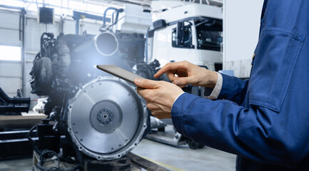 Serviceman with digital tablet on the background of truck engine in the garage	