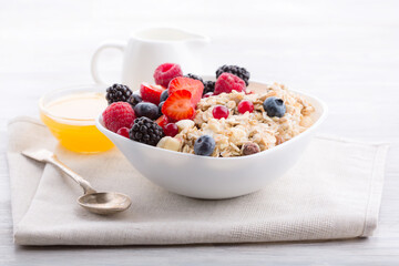 Healthy food concept. Side view photo of oatmeal with fresh berries in white bowl and honey on light wooden table