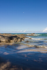beach and rocks and the sea with waves transparent water clouds on the sky