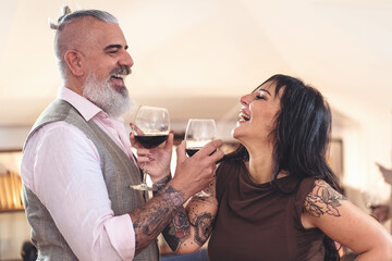 Two middle-aged tattooed lovers toasting wine glasses - Powered by Adobe