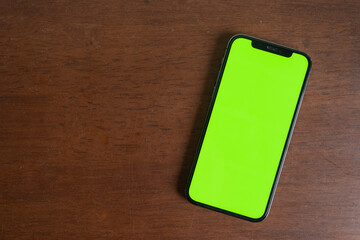 A top view of smartphone with green screen template for social media, web or app mock up. Oak wood background