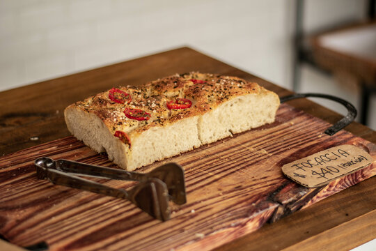 focaccia con tomates cherris y oregano sobre tabla de madera en panaderia, con pinza y bolsa de madera